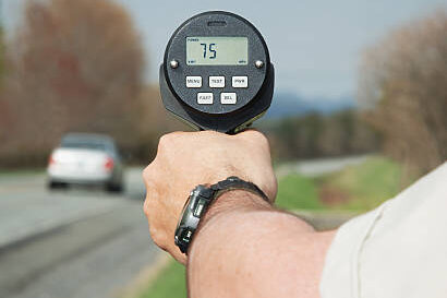 Police officer holding a speed radar. Car speeding at 75 mph.